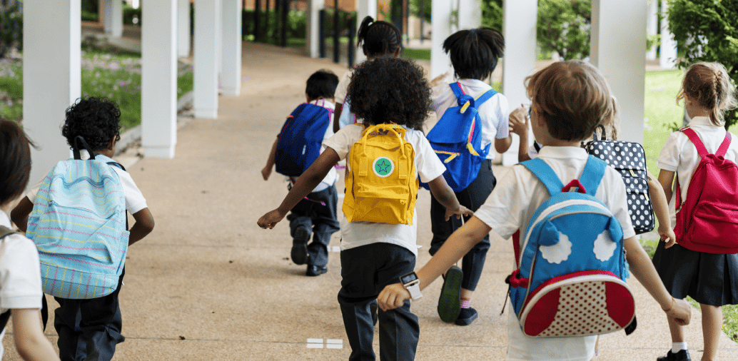 Group of young children wearing backpacks, walking together in a covered pathway.
