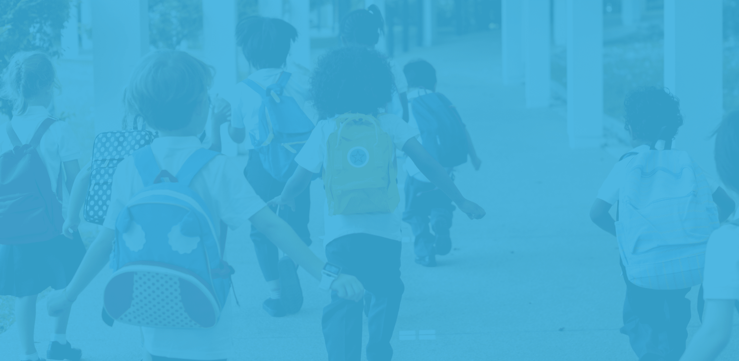 Group of school children with backpacks walking under a covered walkway.