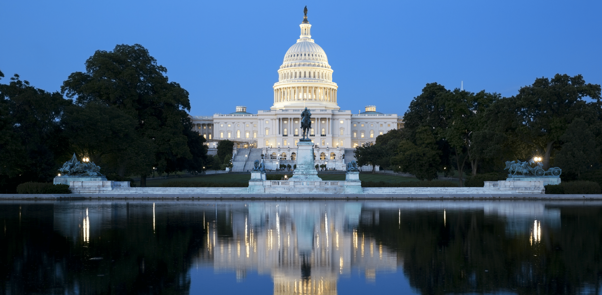 Evening view of the United States Capitol building in Washington, D.C., with its reflection visible in a body of water in the foreground.