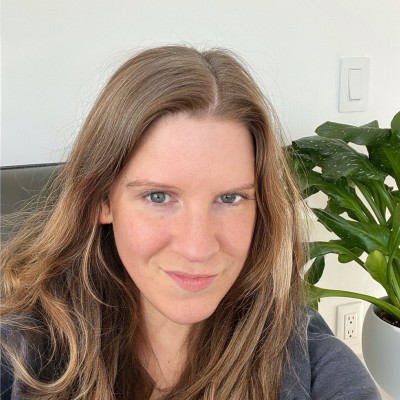 Portrait of Kim Voll, smiling with long hair and a plant in the background.