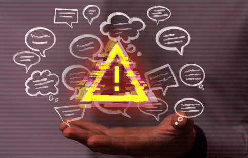 Hand holding a digital warning triangle surrounded by speech bubbles, indicating a cautionary alert related to communication.