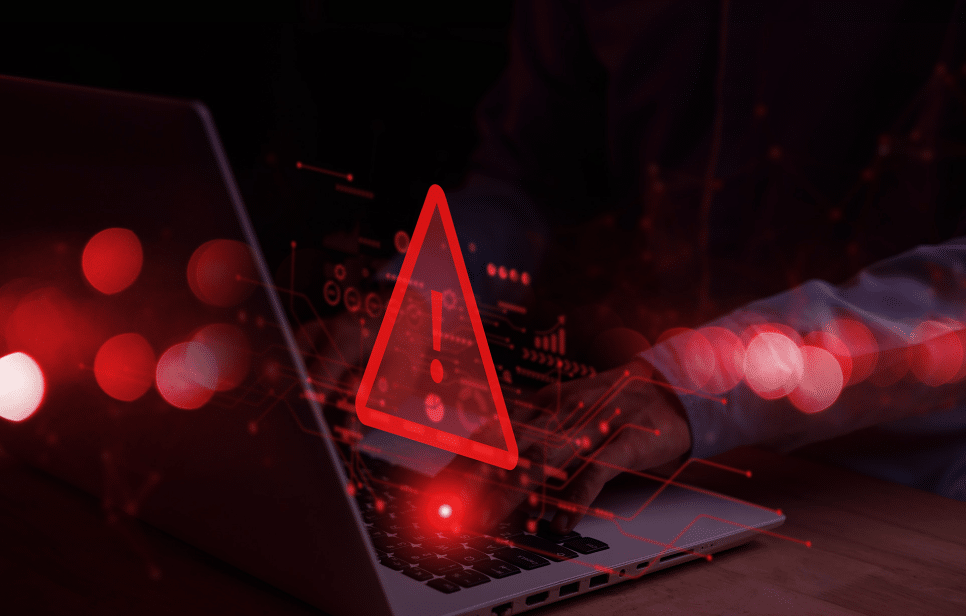 Red warning triangle with an exclamation mark overlayed on a laptop screen with red digital graphics and a person typing.